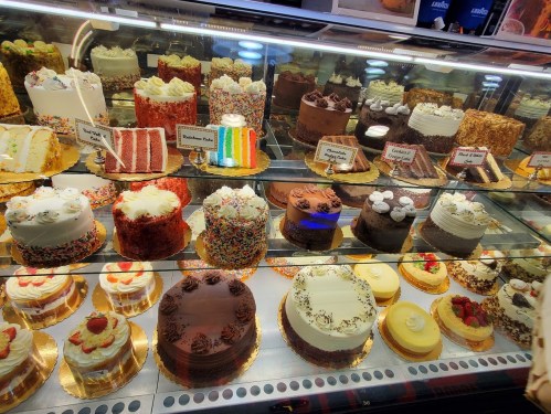 A display case filled with various colorful cakes and desserts, showcasing different flavors and decorations.