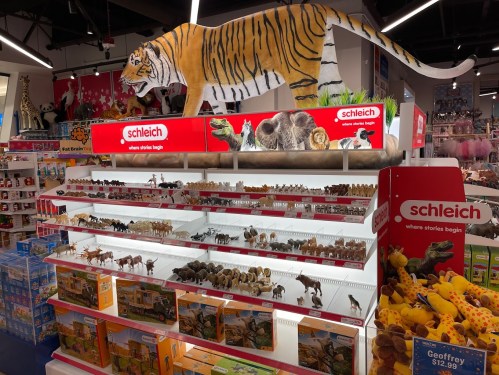 A display of Schleich animal figurines, featuring a large plush tiger on top and various toy animals on shelves below.