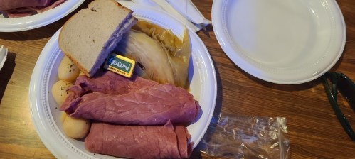 A plate with sliced corned beef, cabbage, potatoes, a slice of bread, and a small butter packet on a wooden table.