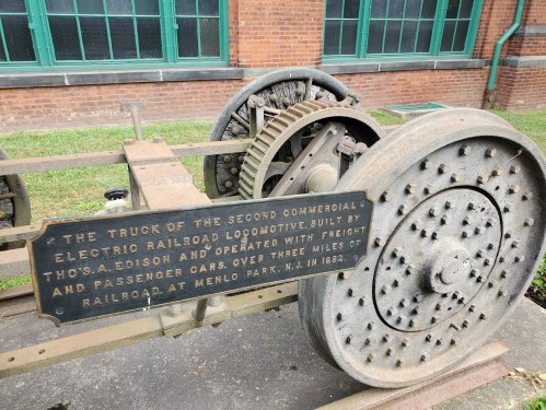 A historic railroad truck with a plaque detailing its significance, displayed outdoors near a brick building.