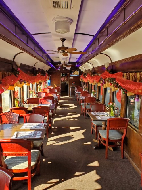 Interior of a decorated train car restaurant with wooden tables, chairs, and festive garlands along the windows.