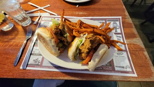Two fried chicken sandwiches with lettuce and tomato, served with a side of sweet potato fries on a restaurant table.