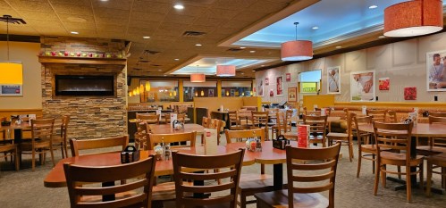 Interior of a cozy restaurant with wooden tables, chairs, and warm lighting, featuring stone accents and colorful decor.
