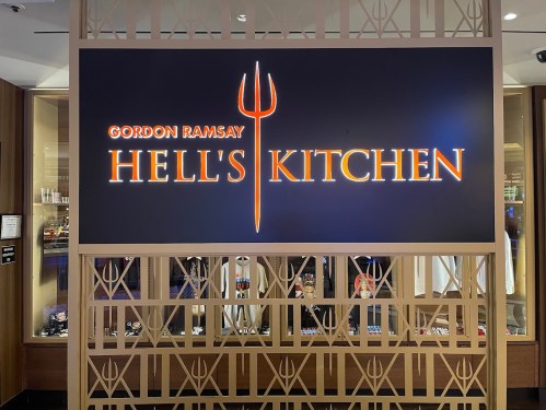 Sign for Gordon Ramsay's Hell's Kitchen, featuring a trident logo and bold orange lettering on a dark background.