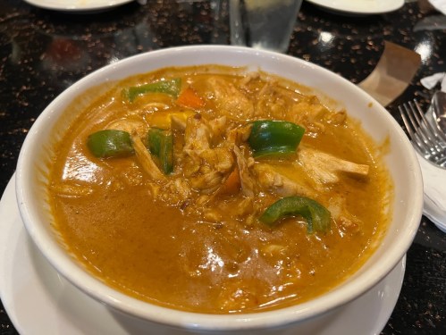 A bowl of chicken curry with green bell peppers in a rich, spicy sauce, served on a black table.