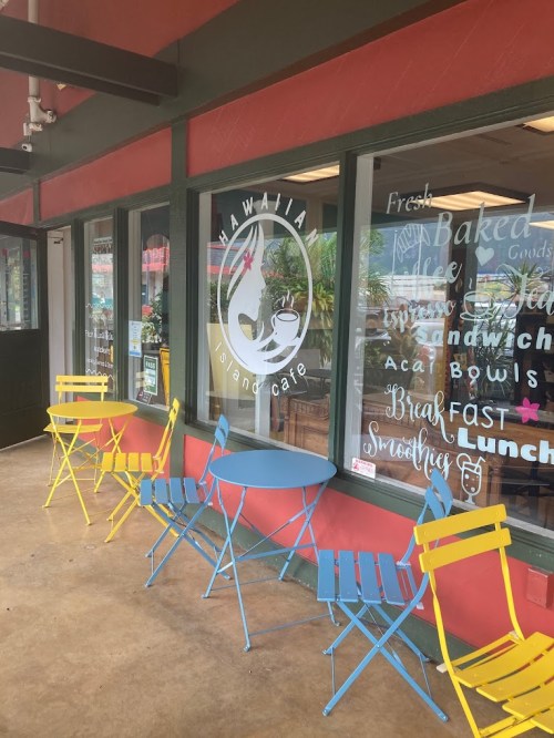 Exterior of Hawaii Island Cafe featuring colorful chairs and a large window with the cafe's logo and menu items.