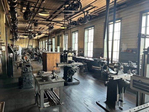 A spacious workshop filled with various vintage machines and tools, illuminated by natural light from large windows.