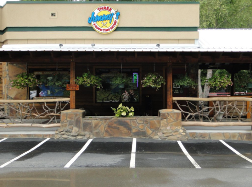 Exterior of a rustic restaurant with a sign reading "Three Jenny's," featuring hanging plants and a stone patio.