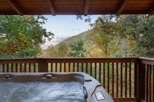 A hot tub on a wooden deck overlooks a scenic view of colorful autumn trees and rolling hills.