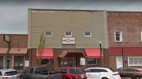 A two-story building with a sign reading "ONE 22 WEST" and red awnings, surrounded by parked cars.