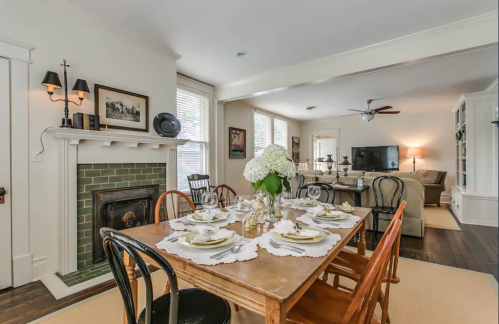 A cozy dining room with a wooden table set for a meal, featuring a fireplace and a view of a living area.