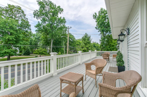 A spacious deck with wicker chairs and a table, surrounded by green trees and a clear sky.