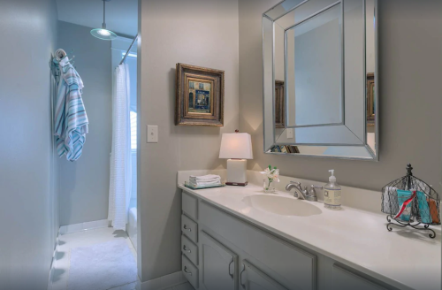 A modern bathroom featuring a white vanity, mirror, lamp, and a shower curtain in the background.