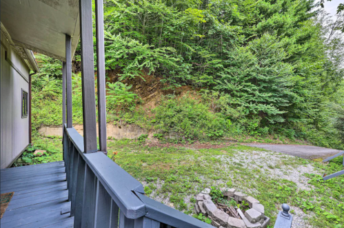 A view from a porch overlooking a grassy area with trees and a stone fire pit.