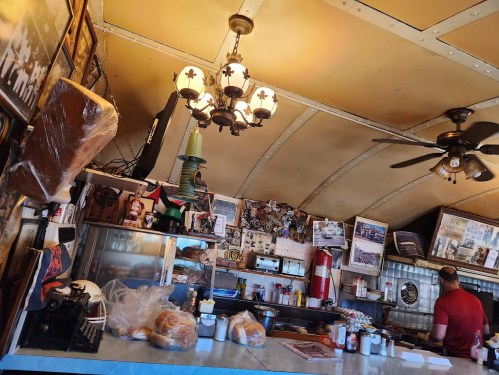 A cozy diner interior with vintage decor, a chandelier, and a counter filled with baked goods and kitchen items.