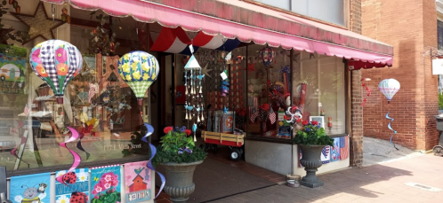 A colorful storefront with hot air balloon decorations, flowers, and festive items displayed in the window.