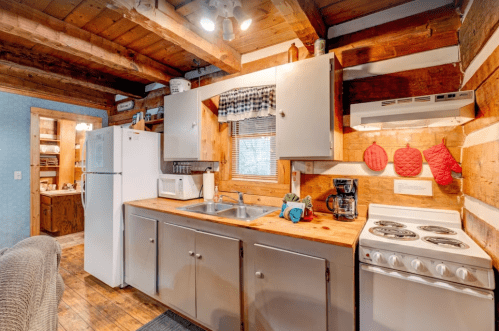 Cozy rustic kitchen with wooden beams, white appliances, and a wooden countertop, featuring a sink and stove.