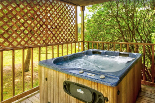 A wooden deck with a hot tub surrounded by greenery and a lattice wall, creating a serene outdoor space.