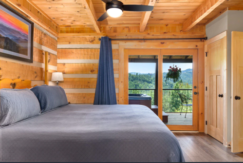 Cozy wooden bedroom with a large bed, a fan, and a view of mountains through sliding glass doors.