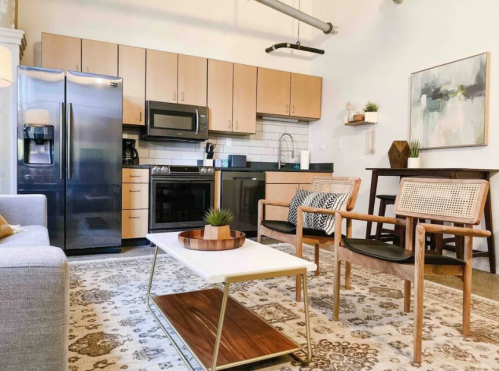 Modern kitchen and living area featuring sleek appliances, wooden furniture, and a decorative rug.