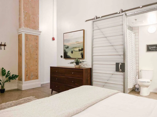 A cozy bedroom with a wooden dresser, artwork, and a sliding barn door leading to a bathroom.
