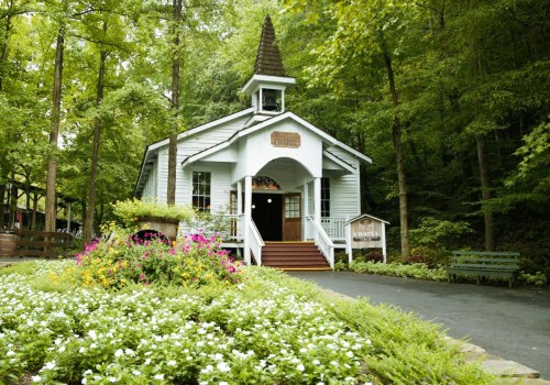 A charming white chapel surrounded by lush greenery and colorful flowers, set in a serene forested area.