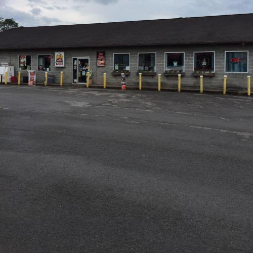 A small convenience store with multiple windows and signs, set against a cloudy sky and empty parking lot.