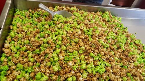 A large tray filled with a mix of green and caramel popcorn, with a scoop resting on top.