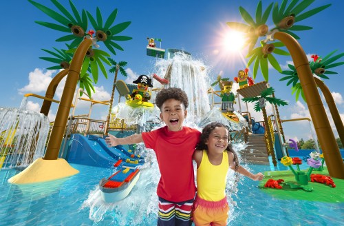 Two joyful children play in a vibrant water park, surrounded by slides, waterfalls, and colorful palm trees.