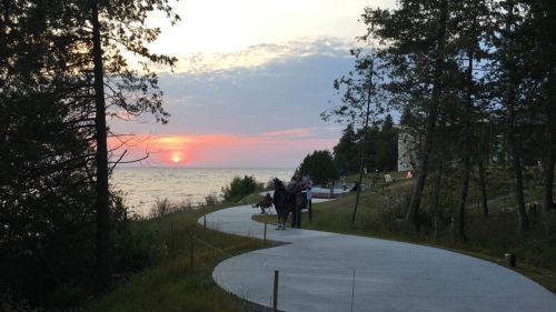 A winding path by the water at sunset, with people walking and trees lining the shore.