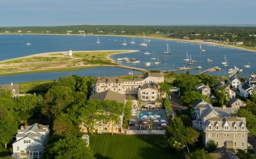 Aerial view of a coastal town with boats in the water, sandy shores, and lush greenery surrounding buildings.
