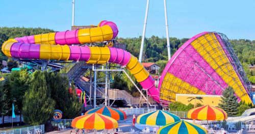 Colorful water slides and a large amusement park ride surrounded by umbrellas and trees on a sunny day.
