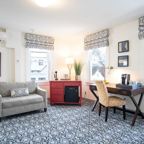 Cozy room featuring a gray sofa, red cabinet, desk with chair, and large windows with patterned curtains.