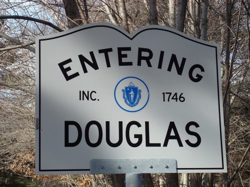 Sign reading "Entering Douglas, Inc. 1746" with a blue Massachusetts state emblem, surrounded by trees.