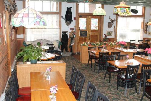 Cozy restaurant interior with wooden tables, black chairs, floral decorations, and rustic decor including a bear statue.