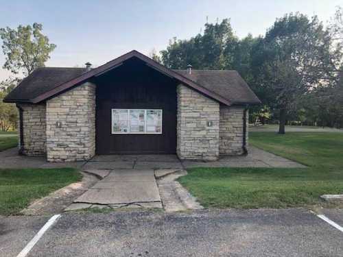 A stone building with a wooden roof, surrounded by grass and trees, featuring informational posters on the front.