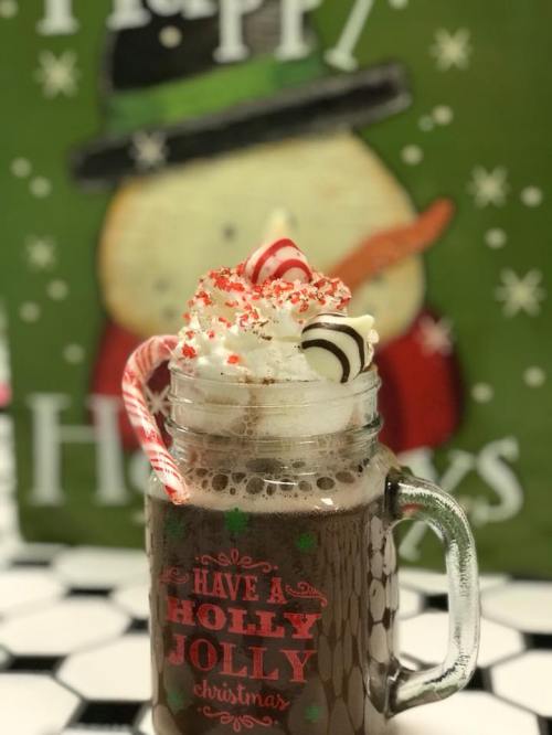 A festive mug filled with hot chocolate, topped with whipped cream, candy canes, and red sprinkles, against a holiday backdrop.