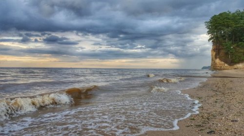 A serene beach scene with gentle waves, sandy shore, and a cloudy sky above a distant cliff.