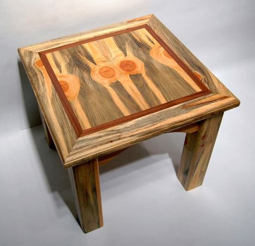 A square wooden table with a unique patterned top and contrasting wood trim, showcasing natural grain and texture.