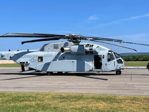 A military helicopter on a tarmac, with a clear blue sky in the background and grass in the foreground.