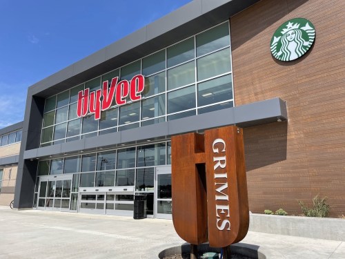 Exterior of a Hy-Vee store with a Starbucks sign, featuring a modern design and a "Grimes" monument in front.