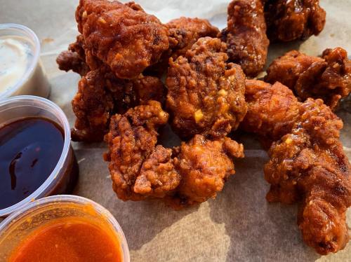 A pile of crispy fried chicken wings with three dipping sauces on the side, resting on parchment paper.