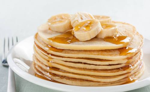 A stack of pancakes topped with banana slices and drizzled with syrup on a white plate.