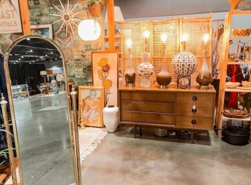 A vintage-inspired display featuring a mirror, dresser, decorative lamps, and various art pieces in a stylish setting.