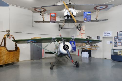 Two vintage airplanes displayed in a museum, with informational posters and a hot air balloon basket in the background.