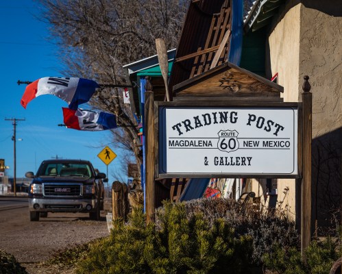 Sign for a trading post and gallery in Magdalena, New Mexico, with flags and a truck parked nearby.