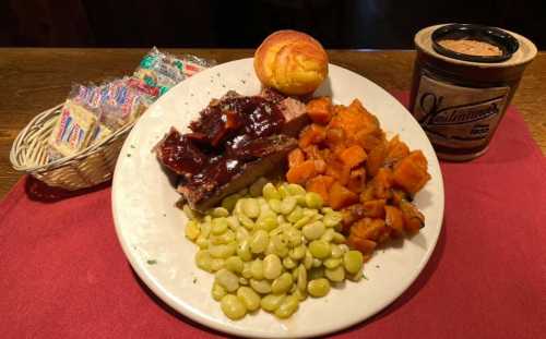 A plate of barbecue meatloaf with sauce, sweet potatoes, lima beans, cornbread, and a basket of candies.