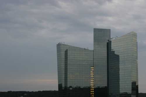 A modern glass building reflecting a cloudy sky, with multiple angular sections and illuminated windows.