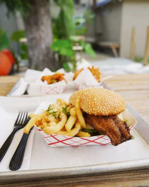 A sesame seed bun with a piece of fried fish, served with crinkle-cut fries on a tray.