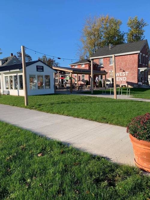 A sunny outdoor area with a grassy space, a white building, and a brick building labeled "WEST END" in the background.